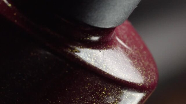 Macro close up of nail polish bottle with black cap and glossy red lacquer around bottle neck revealing cosmetic packaging details with shallow focus and soft lighting