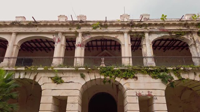 Low angle view of historic Hacienda Oacalco facade featuring weathered colonial arches, balconies and climbing vegetation during daytime in Morelos, Mexico