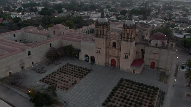 Aerial drone view of Santo Domingo de Guzman Church and surrounding historic center illuminated by soft evening light in Oaxaca City, Mexico at dusk.