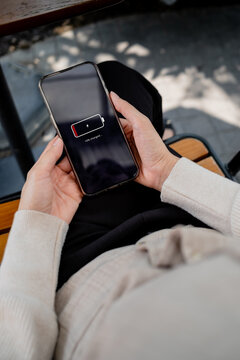 Close-up of a woman holding a smartphone showing a low battery warning at home. Ideal for mobile charging, battery life, technology, productivity and lifestyle concepts.