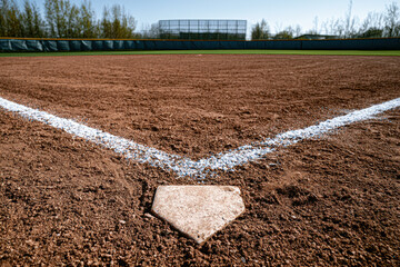 Fototapeta premium Baseball diamond viewed from home plate, empty field with bleachers and trees in the background on a clear day.