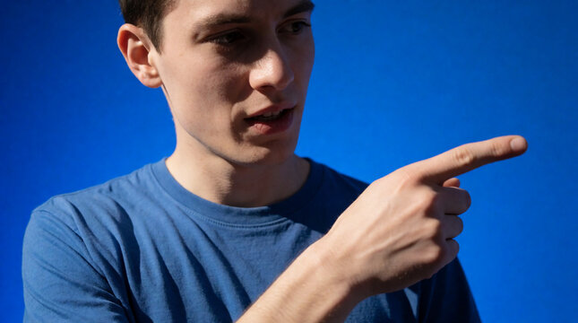 Young man in a blue t-shirt pointing his finger to the side