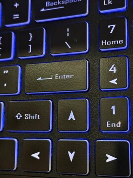 Close-up of backlit laptop keyboard with blue led lighting showing enter and shift keys, keyboard