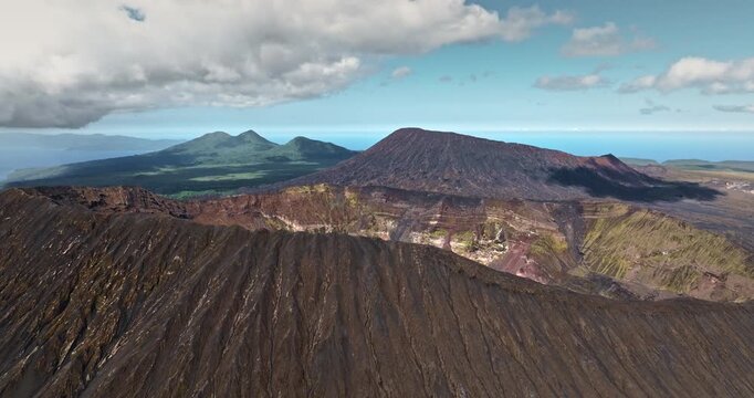 Benbow and Marum volcano craters and caldera against a cloudy blue sky and distant ocean. Rugged volcanic landscape of Ambrym Island, Vanuatu. Amazing remote nature landscape. Aerial drone flight