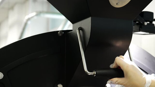 Operator opens the discharge lever of a commercial coffee roaster before releasing freshly roasted beans. Close-up of coffee roasting equipment in food production.