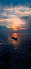 Obraz premium A powerful and dramatic seascape showing a lone fishing boat silhouette on a dark ocean beneath a dramatic sunset sky with vivid orange and red hues between dark moody storm clouds, evoking solitude.