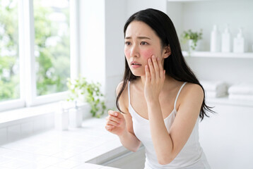 Fototapeta premium 頬の赤み・赤ら顔・酒さなどの肌荒れを気にする若い日本人女性のスキンケアと敏感肌トラブルを表現した美容イメージ