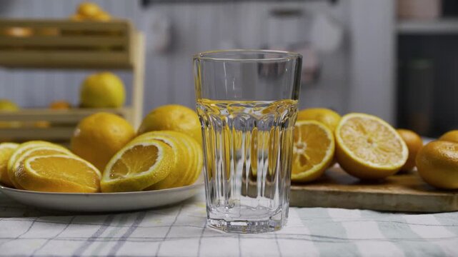 Stream of orange juice pouring into glass and splashing near fruit in slow motion