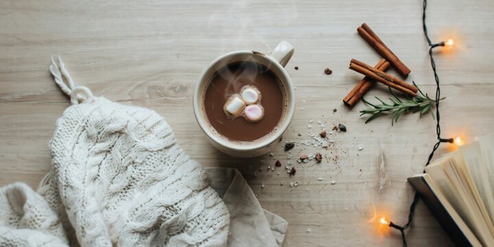 Cozy winter flat lay with hot chocolate mug, knitted sweater, and sparkling lights. Cozy Hot Chocolate with Marshmallows and Cinnamon.