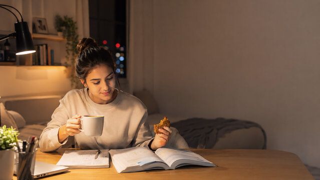 Young woman taking a coffee break while studying at night in cozy home workspace with copy space