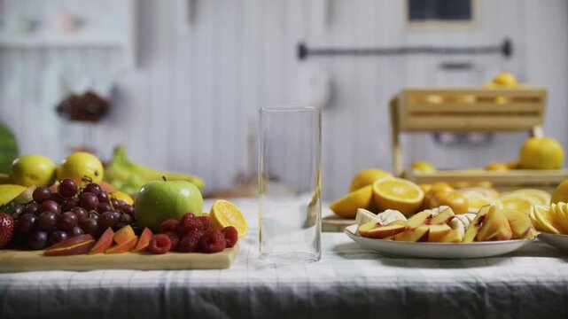 Empty glass between plates of oranges and other fruit at kitchen counter, medium shot