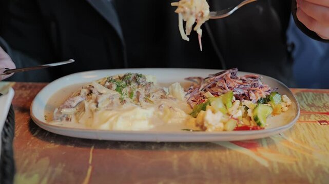 Person prepares to enjoy creamy beef stroganoff with mashed potatoes and fresh salads indoors.