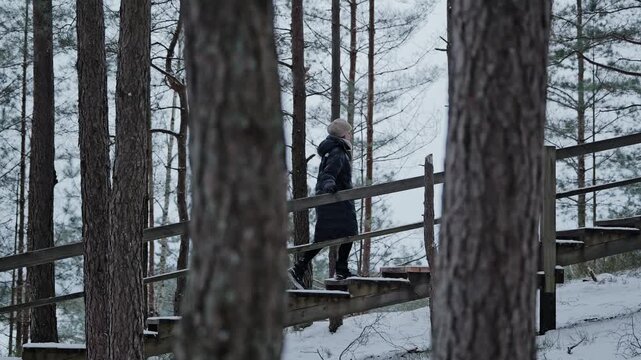 Cinematic side tracking shot of a woman climbing snowy wooden stairs Blue hills