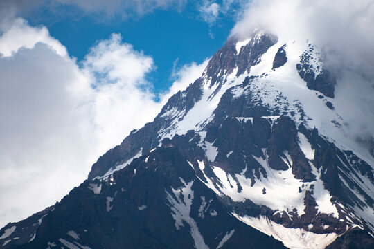 High snow peak of Mount Kazbek against blue sky and clouds in Georgia with copy space