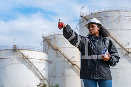 Engineers wearing safety gear, including hard hats examining survey a large blueprint tablet standing industrial facility gas or oil refinery engaged in a job requires high safety standards concept.	