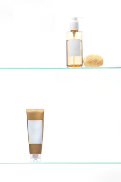 Organic beauty products. The amber liquid soap/oil and matte tube with blank labels are paired with a textured sponge, highlighting clean beauty and spa aesthetics on glass.