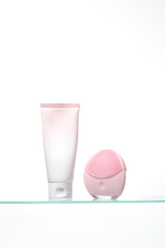 Skincare essentials displayed with a soft pink cleanser tube and an electronic silicone face brush. 