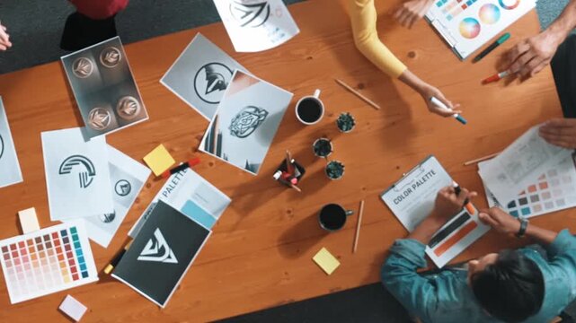 Top view of designer writing and designing logo graphic at meeting. Closeup of business man working on colored palettes and writing idea on sticky notes on table with equipment and paper. Symposium.