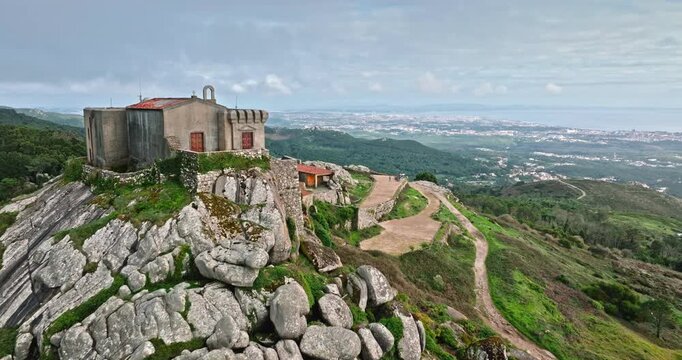 Peninha Sanctuary in Sintra Cascais, an ancient hermitage and chapel complex. Standing on a rocky peak with a dramatic aerial view of the surrounding Natural Park in Portugal. Drone flight shot