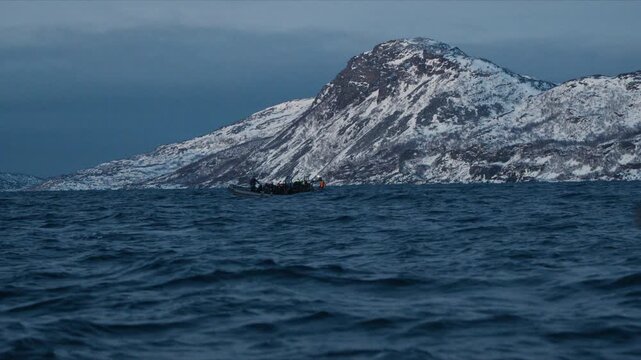 Expedition boat crosses Arctic fjord below snowy Norway mountain landscape