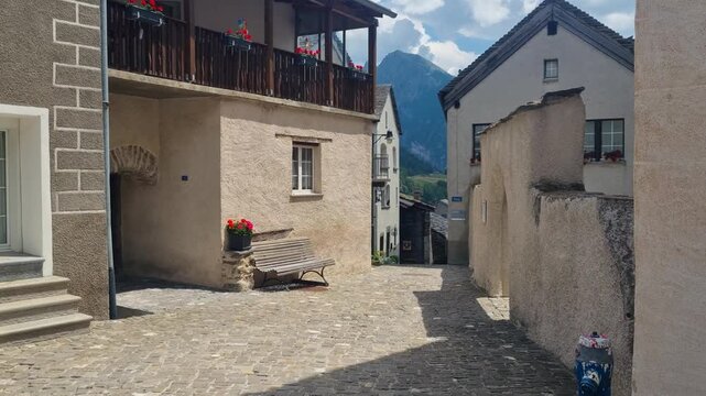 Historic village street in Simplon Dorf, Switzerland, showcasing a narrow cobblestone path, traditional stone houses, and authentic Alpine architecture in a charming mountain setting