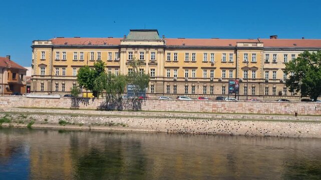 Panning view over the former Banovina building in Ni&scaron;, Serbia, now home to the Nikola Tesla University Library, featuring a historic yellow fa&ccedil;ade, monumental architecture, and a the Nisava river