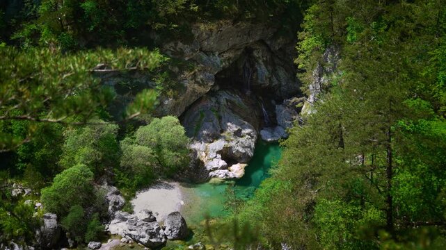 Natural waterfall rushing into a transparent green water basin surrounded by alpine cliffs at Pozze Smeraldine