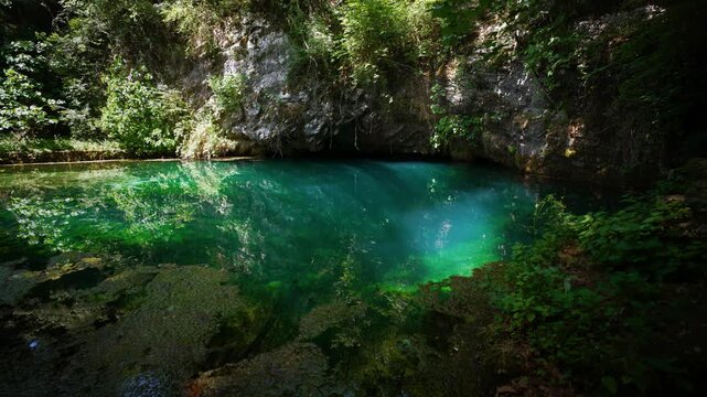Crystal clear turquoise water basin, underwater sun rays and mossy rocks at Gorgazzo source, Italy