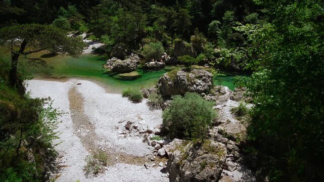 Winding emerald mountain stream flowing past forested valley slopes and white pebbles at Pozze Smeraldine.