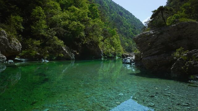 Hidden emerald green water hole surrounded by wild forest and steep grey rocks at Pozze Smeraldine, Italy.