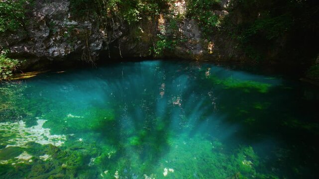 Natural turquoise clear pond, sun rays cutting through water and green algae at Gorgazzo karst spring