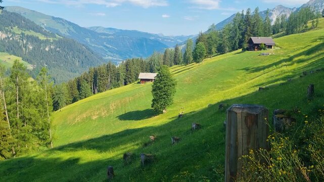 Stunning panoramic view of the Swiss Alps in the Bernese Oberland near Lenk on a sunny summer day. Lush green alpine meadows, traditional farming chalets, and breathtaking mountain scenery