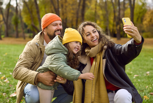 Family parents mother father daughter taking selfie. In an autumn park, parents hold a phone as the child leans in capturing candid smiles and warm light. Concept of smartphone family bonding.