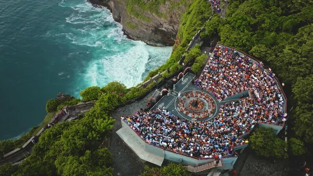 Balinese Kecak fire dance performance, cultural tourism, and travel in Uluwatu, Bali. Large audience people watching a traditional show inside a cliffside amphitheater, Indian Ocean seen from above