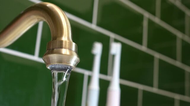 Water flowing from a vintage bronze faucet against a green tiled wall background. Concert - payment of utility bills for water, water consumption in the apartment, clean water from the tap. High quali
