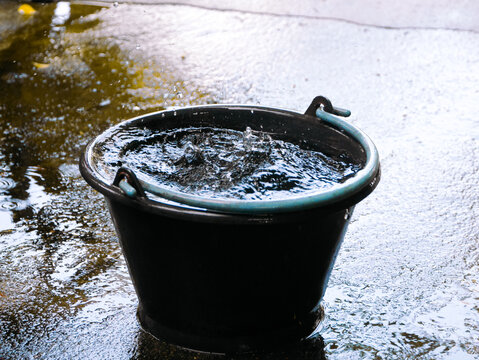Heavy precipitation drops fall into a dark container, demonstrating meteorological rainwater harvesting methods, domestic hydrology conservation, and natural liquid resource sustainability