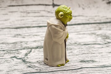 Fototapeta premium Detailed green Yoda figure stands on a textured surface, wearing a tan robe and holding a staff, exuding wisdom and tranquility