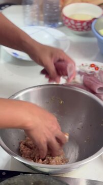 Home chef hands preparing stuffed squid, mixing seasoned minced pork inside stainless steel bowl, holding raw seafood tube, cooking traditional Asian recipe inside domestic kitchen.