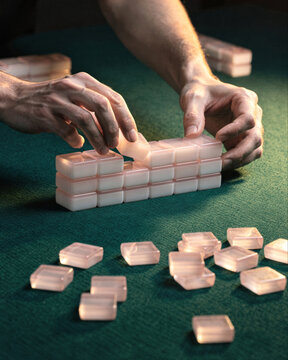 Hands Stacking Mahjong Tiles on Green Felt Table