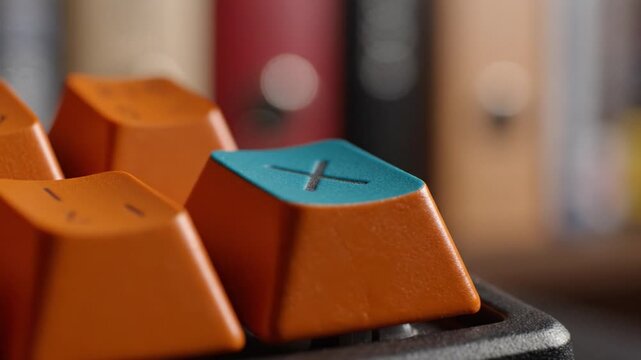 Colorful keyboard keys with a distinctive blue key on a blurred background of books, showcasing an artistic and modern design aesthetic in technology.