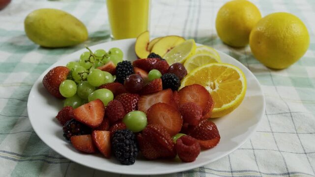 Plate filled with delicious fruit near cup of orange juice - tracking shot