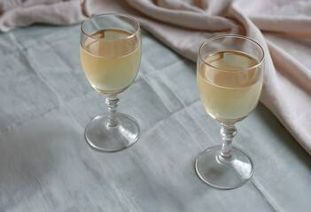 Obraz premium Two glasses of white wine on a light green tablecloth with a beige napkin, elegant beverage and dining concept, this arrangement suggests an elegant dining experience or a celebratory event