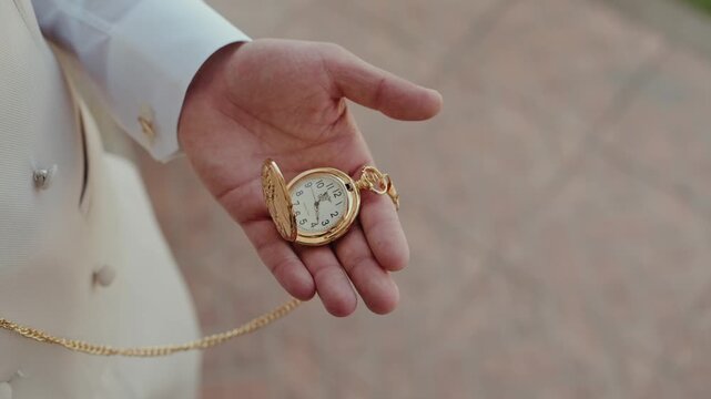 Man in cream suit holding an engraved gold pocket watch with chain