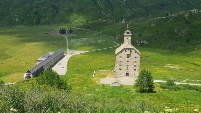 Sunny summer view of the historic Old Hospice (Alter Spittel) and Barralhaus on Switzerland's Simplon Pass, surrounded by lush green meadows and breathtaking alpine scenery