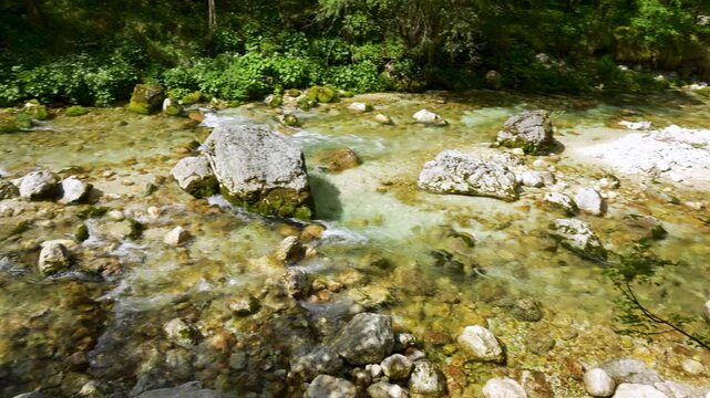 Clear alpine creek at &Scaron;unik Water Grove in Lepena Valley, Slovenia, with shallow turquoise water, white stones and green forest shade.
