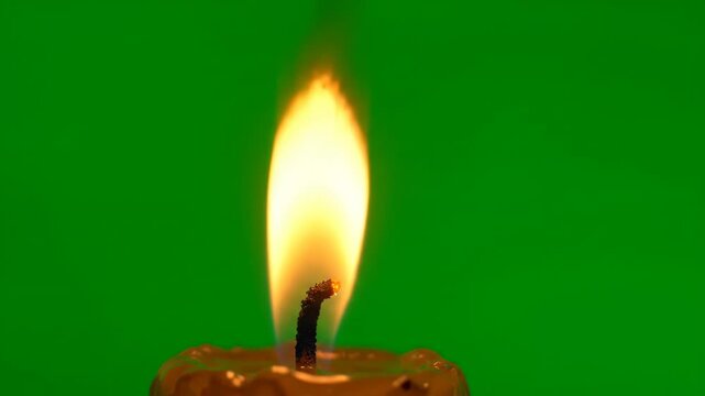 Candle Flame Burning: A close-up of a single candle flame, burning brightly against a vibrant green background, symbolizing warmth and light.