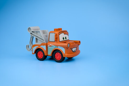 A Tow Mater toy from the side with its towing hook, brown body, and contrasting red wheels against a light blue background on Jul 25, 2026 in Jakarta, Indonesia