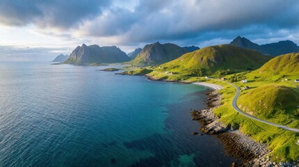Naklejka premium Aerial view of Norway coastline with turquoise water, green grassy mountains. Winding road follows rocky shore near small houses. Cloudy sky above dramatic fjord landscape during summer day. Travel