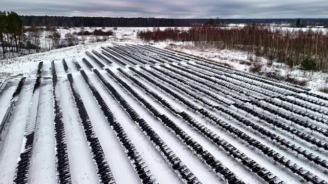 Aerial view of rows of solar panels covered in snow in a rural landscape in Latvia.