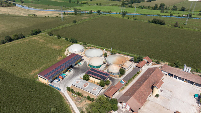 Aerial view of a biomethane production facility with circular digesters, solar panels, and agricultural buildings surrounded by green fields in Tavazzano con Villavesco, Lombardy, Italy.